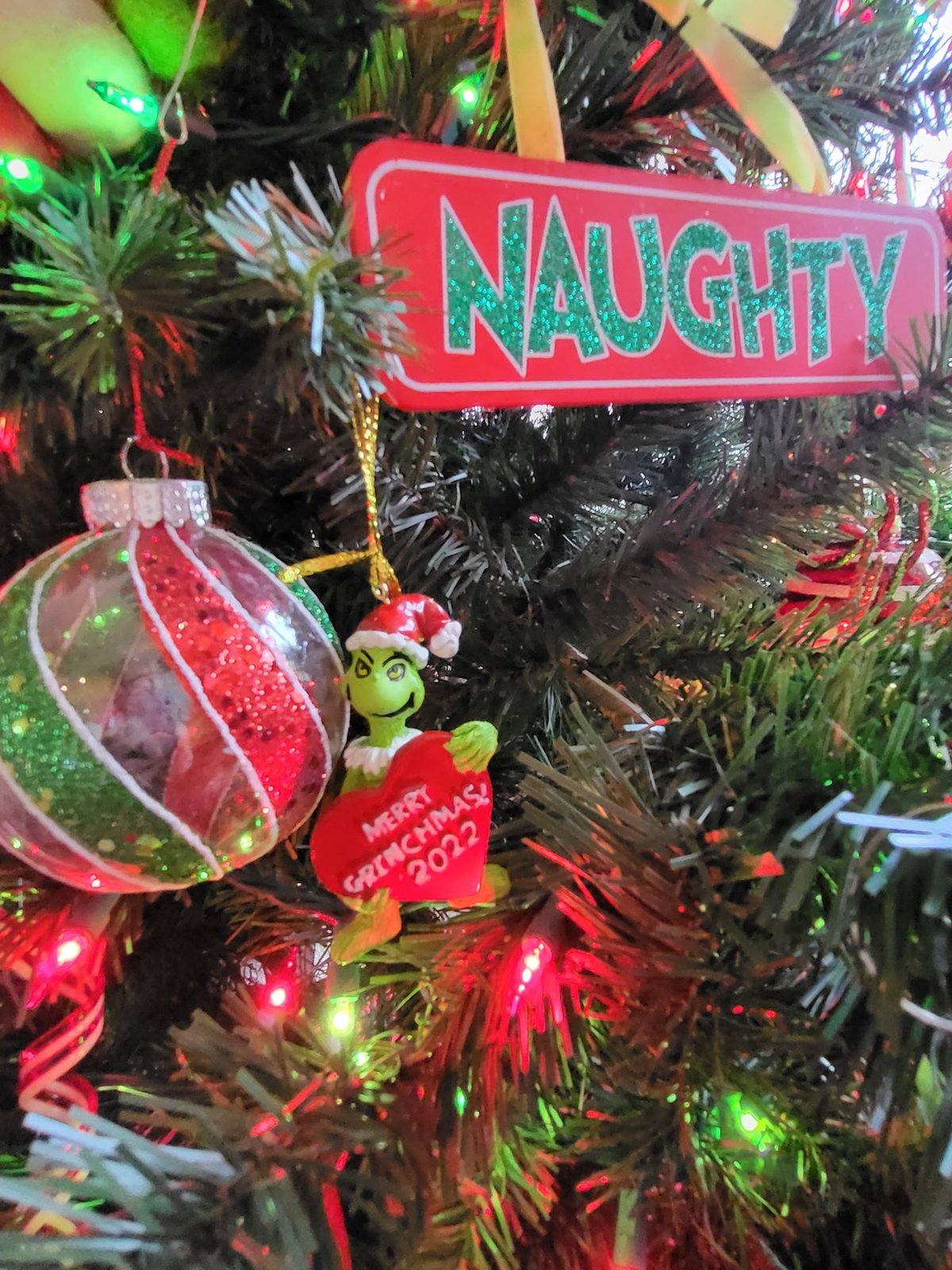 Naughty sign and a striped ball ornament on a lit tree