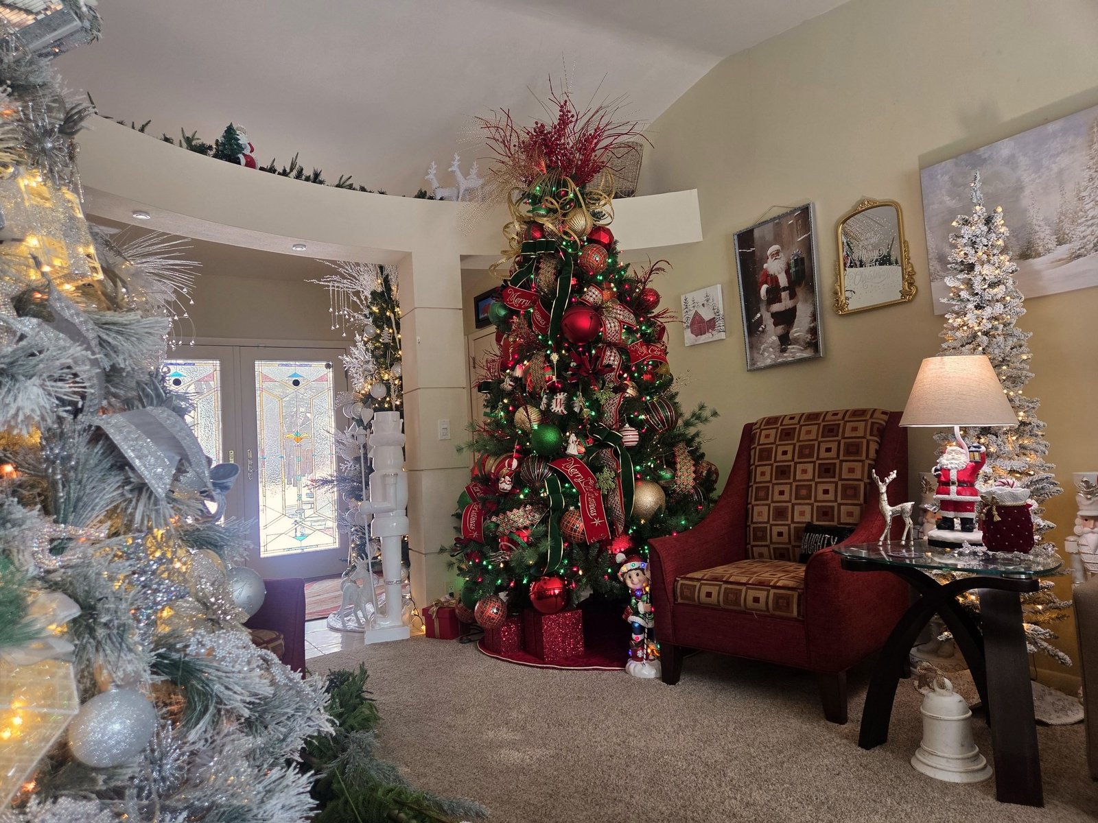 Red and green decorated Christmas tree beside flocked white trees in a front room