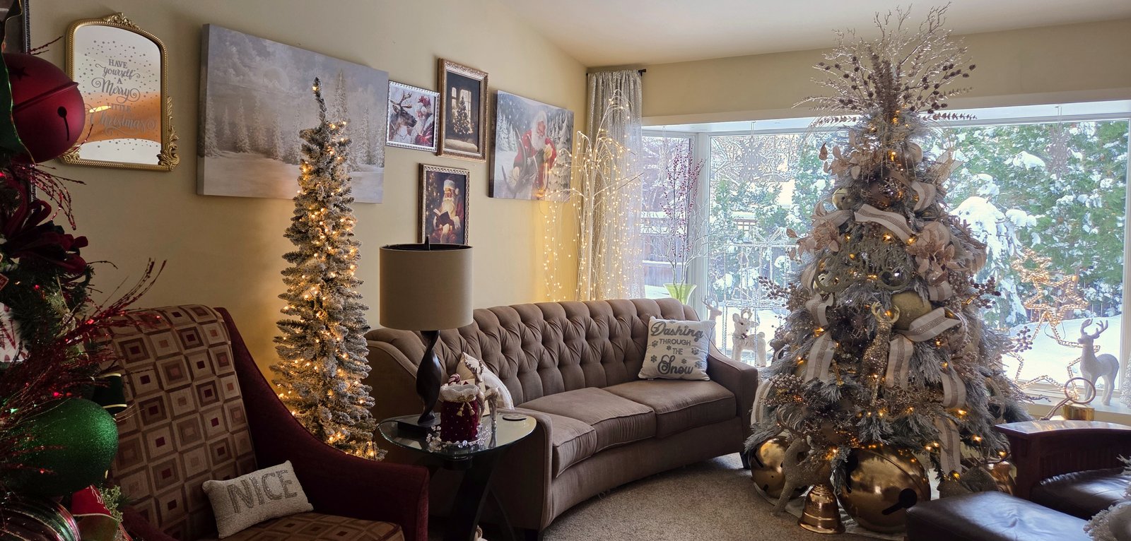 Living room with decorated Christmas trees, a sofa and lamp, and snow through the window