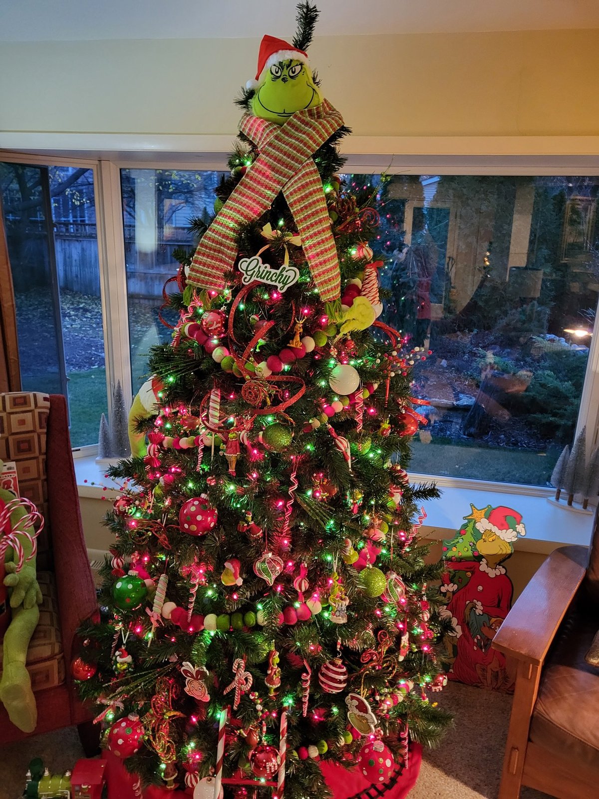 Grinch themed Christmas tree with a striped hat topper beside a window