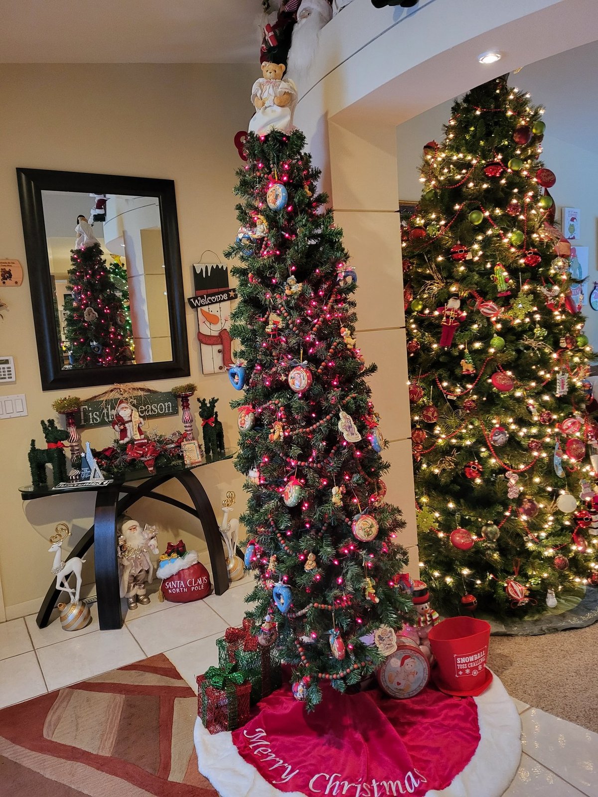 Decorated Christmas trees beside a mirrored console in a hallway