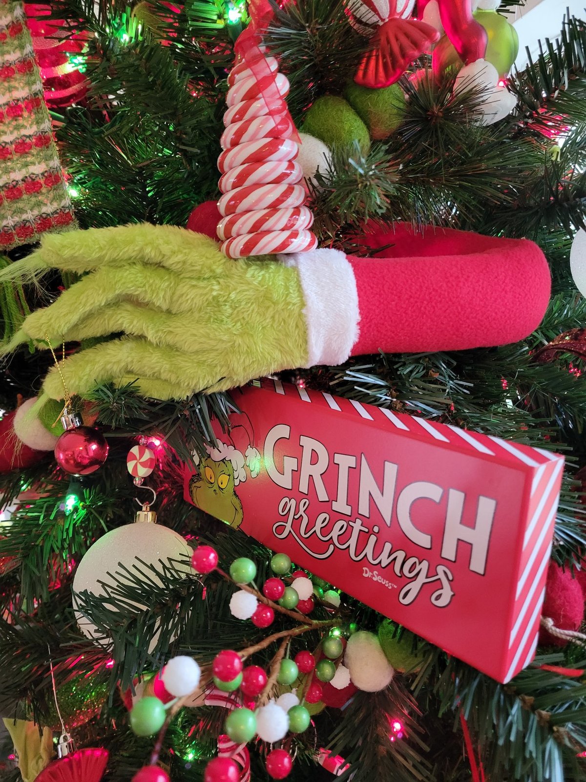 Close view of a Grinch greetings sign among candy cane picks on a tree