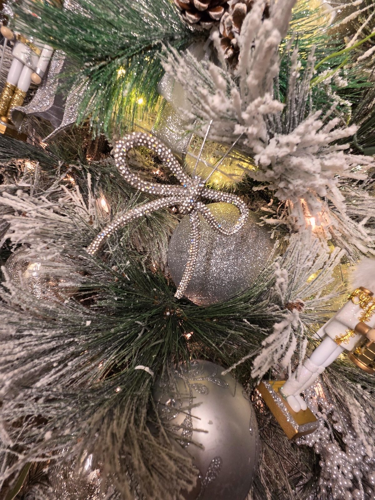 Close view of a beaded silver ornament and pearl ribbon on a flocked branch