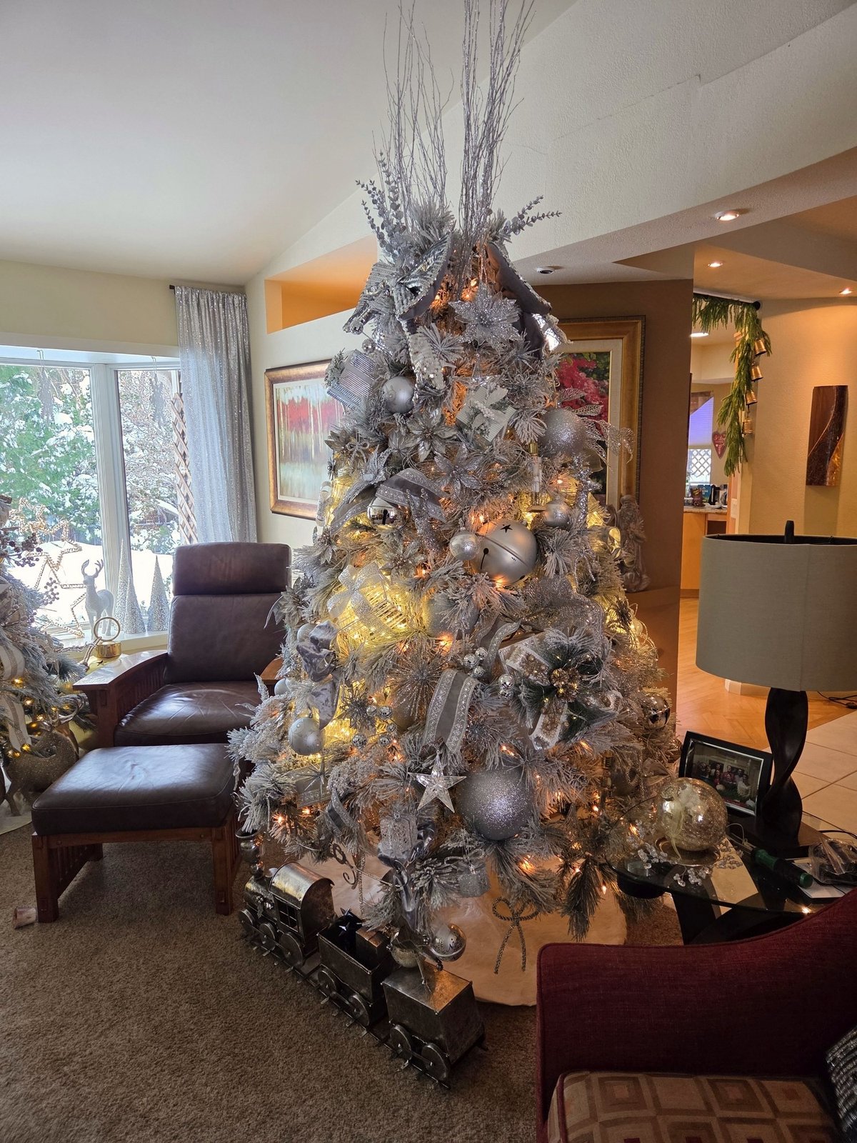 Flocked Christmas tree with silver and gold ornaments beside a window