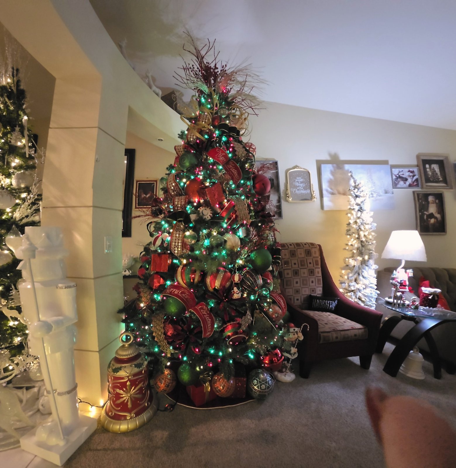 Red and gold Christmas tree in a living room beside a flocked white tree