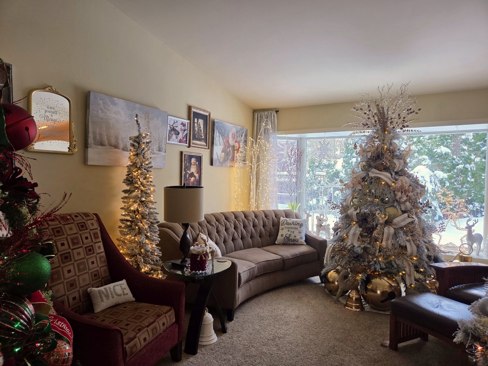 Flocked Christmas trees in a living room with snow visible through the window