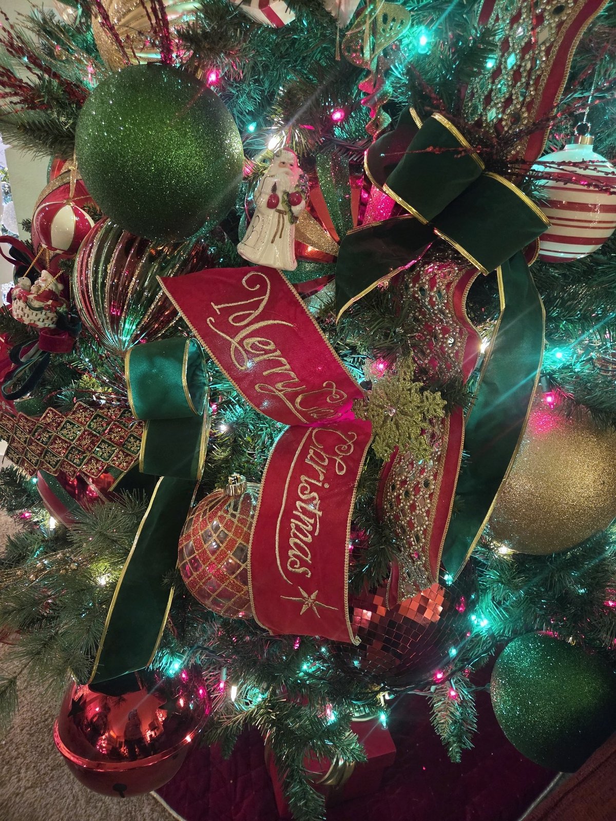 Close view of red Merry Christmas ribbon and gold ornaments on a decorated tree