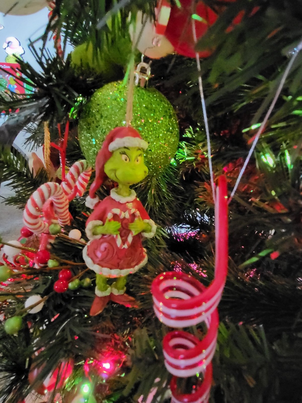 Grinch character ornament hanging beside a candy cane pick